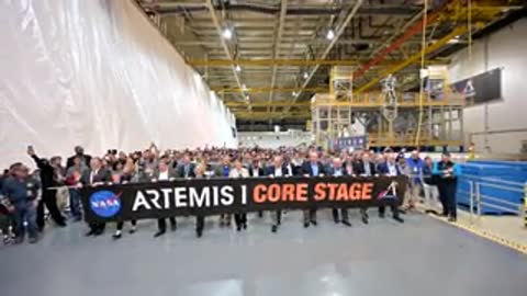Crowd holding Artemis I Core Stage banner inside warehouse