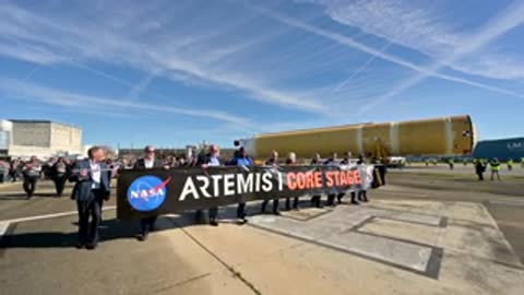 People walking behind rocket stage transport holding banner