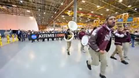 Marching band entering indoor warehouse space with instruments