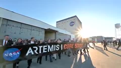 Crowd walking outside building while holding banner in sunlight