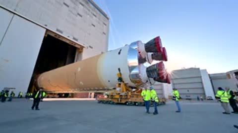 Rocket core stage exiting building on transport vehicle outdoors