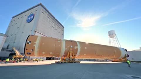 Large orange rocket stage moving past building exterior