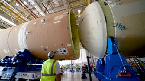 Workers guiding the connection of two large rocket components horizontally.