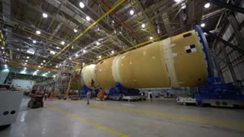 Long horizontal rocket component resting on transport stands in a facility.