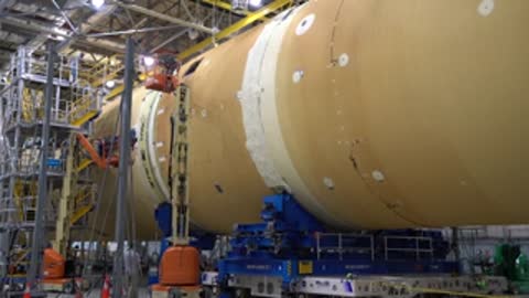 Medium shot of workers near a horizontal rocket component inside a facility.
