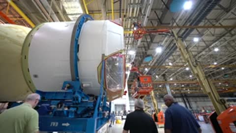 Workers inspecting the end section of a large rocket component on a stand.