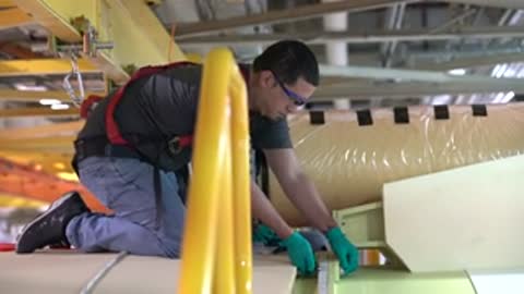Worker kneeling and working on a component structure with tools.