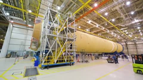 Wide shot of a long horizontal rocket component inside a factory facility.