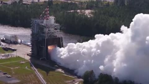 Exterior view of rocket engine test facility billowing heavy white smoke.