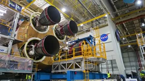 Four rocket engines mounted on a large core stage inside assembly building.
