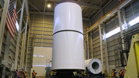 Vertical white cylindrical rocket component standing inside industrial warehouse.