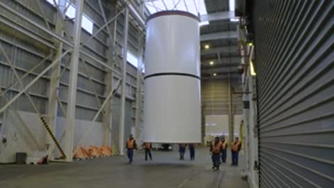 White cylindrical rocket component suspended horizontally inside industrial facility.