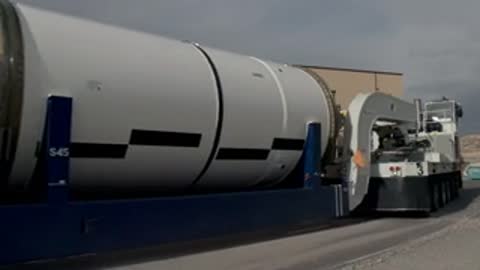 Large white cylindrical component transported horizontally on flatbed truck outdoors.