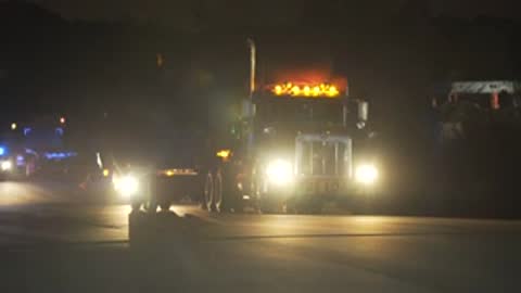 Semi-truck with headlights on driving on road at night.