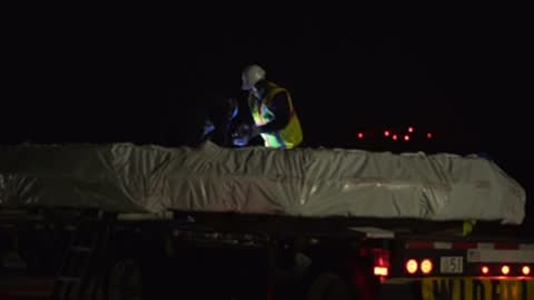 Workers in high-vis vests work on a flatbed truck at night.