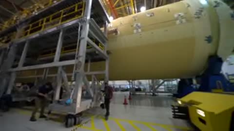 Horizontal rocket component resting on supports as workers prepare it for transport.