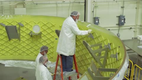 Technicians assemble a large green cylindrical structure indoors.