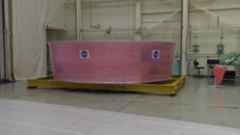 A large pink-wrapped cylindrical component sits on a transport platform indoors.