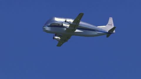 A large cargo aircraft flies low across a blue sky.