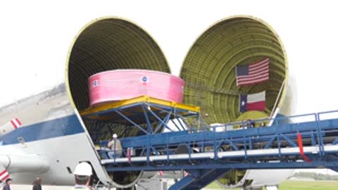 A pink component is loaded into the open nose of a large cargo aircraft.