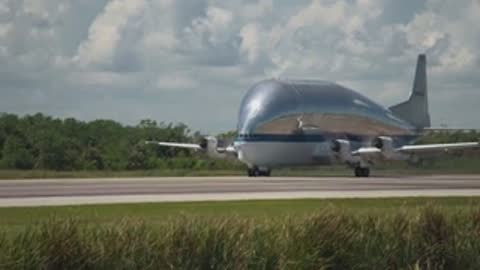 A large cargo aircraft taxis down a runway surrounded by grass.