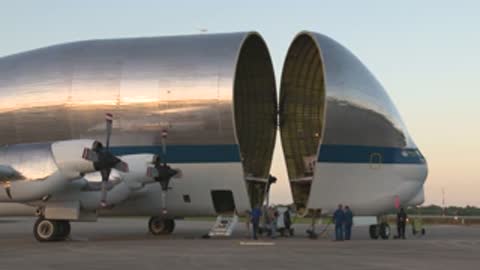 Workers gather around the open nose section of a cargo aircraft parked on the tarmac.