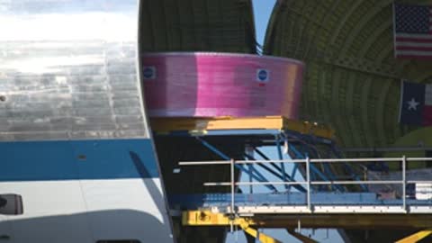 A pink cylindrical component is positioned inside the cargo hold of an aircraft.