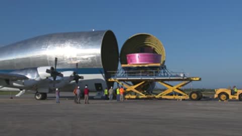 A pink component is being loaded into a cargo aircraft on the tarmac.
