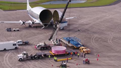 An aerial view shows a cargo aircraft parked on the tarmac with support vehicles.