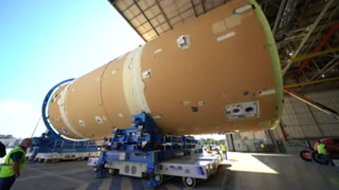 Rocket component resting horizontally on a transport rig inside a facility.