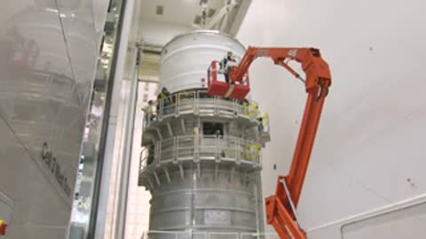 medium shot of orange crane servicing cylindrical rocket part
