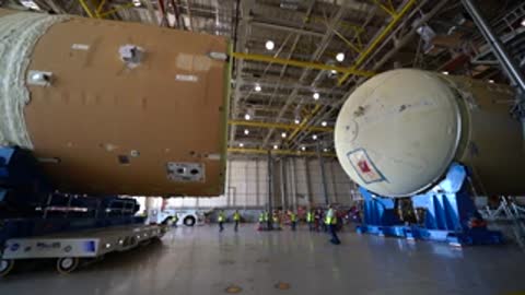 Two rocket components being aligned horizontally inside a large facility.