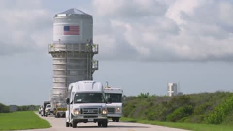 medium shot of transport trucks hauling rocket section along road