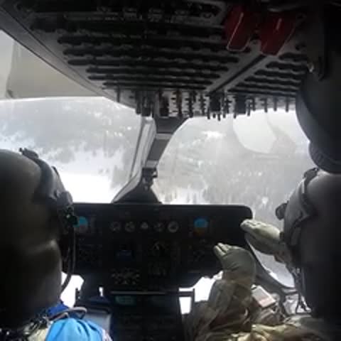 View from inside a helicopter cockpit showing controls and landscape ahead.