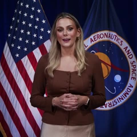 Bethany Stevens speaking in front of US and NASA flags, smiling.