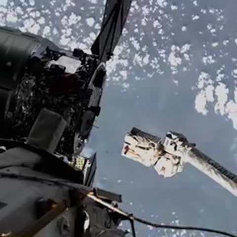 Close-up of spacecraft components and a mechanical arm against Earth background.