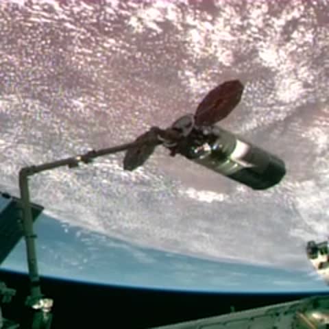 Spacecraft attached to a robotic arm overlooking Earth's curved horizon.