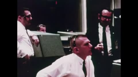 Medium shot of personnel gathered around a console discussing operations