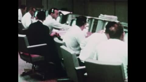 Wide view of the busy Mission Control room with multiple rows of consoles