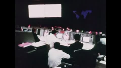 Wide shot of the Mission Control room showing large wall maps and screens