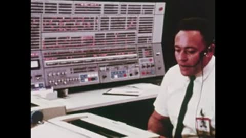 A flight controller working at his console in Mission Control, wearing a headset.