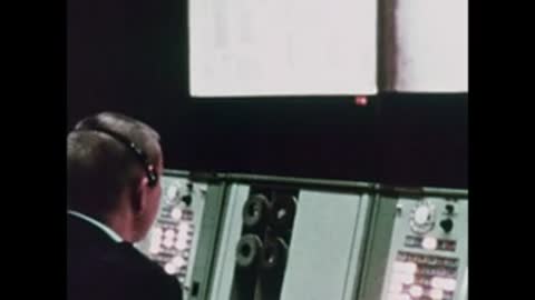 A flight controller viewed from behind, looking at his console in Mission Control.