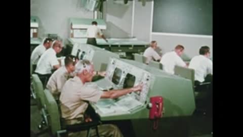 Multiple flight controllers working at their green consoles in Mission Control.
