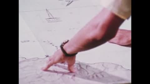 A person's hands and arms gesturing over a map spread out on a table.