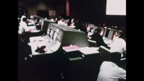 A wide view of the Mission Control room with multiple controllers at their consoles.