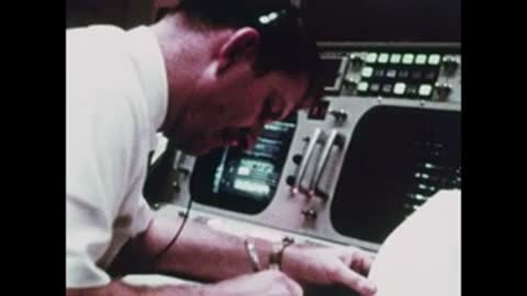 A flight controller leaning forward and writing at his console in Mission Control.