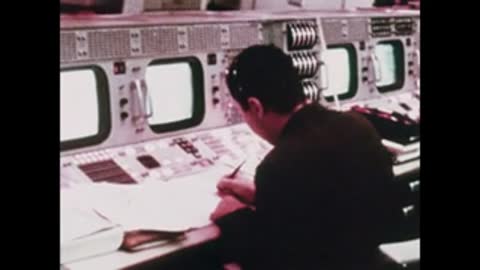 A flight controller working at a complex console in Mission Control, back view.