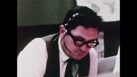 A flight controller wearing glasses and a headset, looking down thoughtfully.