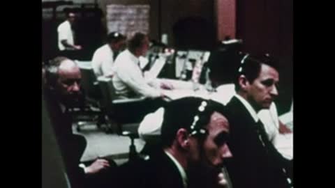 A group of flight controllers sitting and working together in Mission Control room.