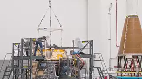 Technicians working around Forward Bay Cover being lowered onto Orion capsule